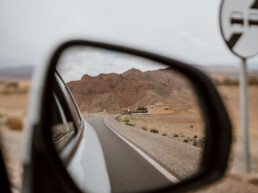 Reverse shot of a road in the middle of Morocco through the right side mirror of the car