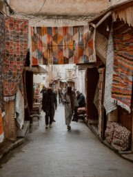 People walk through an archway covered with carpets in the medina of Fez